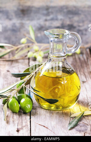 Brocca di olio di oliva con olive branch su un tavolo di legno. Foto Stock