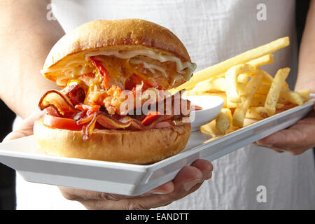 Aragosta principale BLT tomato mayo su una brioche rotolo su una piastra bianca con catchup e patatine fritte persona tenendolo Foto Stock