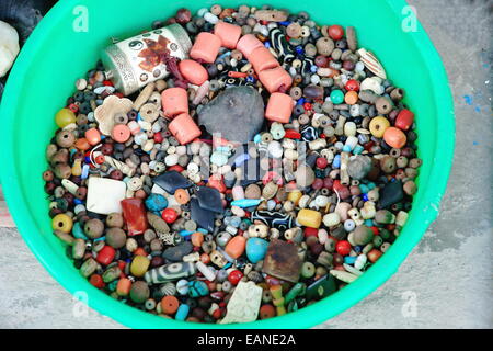Molti colorato e multiforme cordoni di pietra per la collana rendendo impostato su una verde secchio di plastica sul marciapiede di cemento al di fuori di un negozio Foto Stock