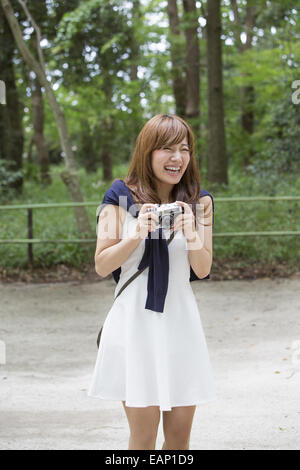 Una donna in un parco di Kyoto tenendo una telecamera, preparazione per scattare le foto. Foto Stock