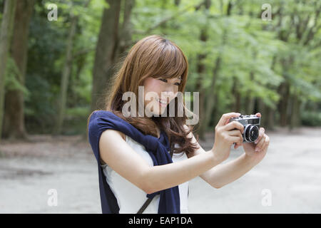 Una donna in un parco di Kyoto tenendo una telecamera, preparazione per scattare le foto. Foto Stock