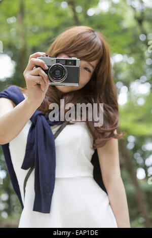 Una donna in un parco di Kyoto tenendo una telecamera, preparazione per scattare le foto. Foto Stock