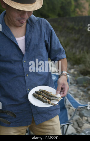 Uomo con un piatto di pesce alla griglia in corrispondenza di un picnic. Foto Stock