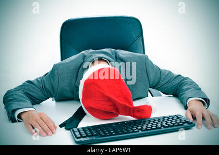 Un uomo in tuta con un cappello da Babbo Natale addormentato nella sua scrivania dopo un ufficio Christmas party Foto Stock