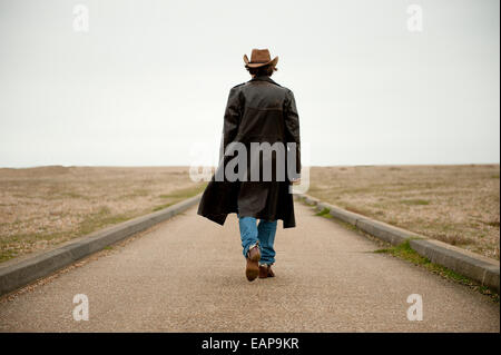 Uomo che indossa lungo nero e il cappello da cowboy, a piedi dalla videocamera verso il lontano orizzonte. Foto Stock