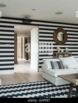 Bianco e nero a strisce pareti in salotto con chevron tappeto a motivi geometrici. Il divano è un Brooklyn 5 pezzo da OKA. Foto Stock
