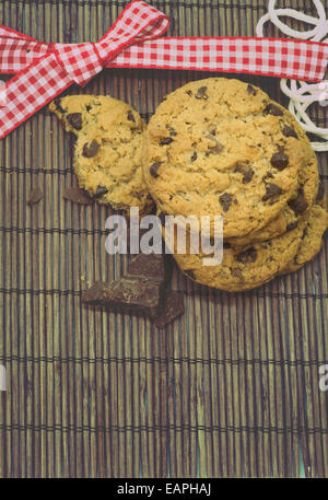 I cookies, aggiungete pezzetti di cioccolato sulla tovaglia bambù rustico, nastro rosso Foto Stock