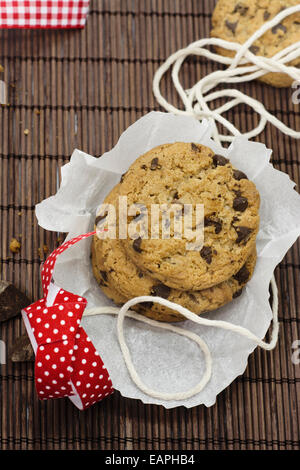 I cookies, aggiungete pezzetti di cioccolato sulla tovaglia bambù rustico, nastro rosso Foto Stock