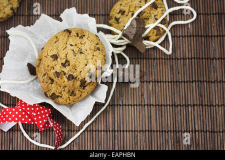 I cookies, aggiungete pezzetti di cioccolato sulla tovaglia bambù rustico, nastro rosso e fiori il coltello Foto Stock