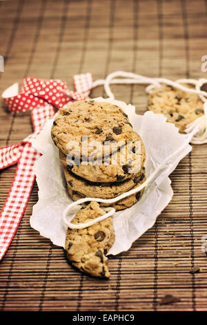 I cookies, aggiungete pezzetti di cioccolato sulla tovaglia bambù rustico, nastro rosso Foto Stock