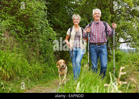Felice coppia senior facendo Nordic Walking con il cane in una foresta Foto Stock