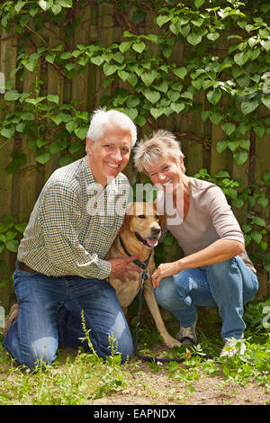 Due senior felice la gente seduta con un cane in un giardino Foto Stock