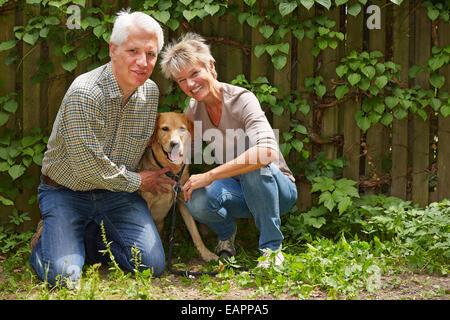 Uomo anziano e sorridente donna seduta con il loro cane in un giardino Foto Stock