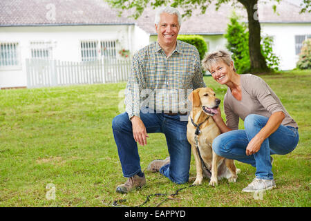 Due senior sorridente gente seduta con il cane davanti alla loro casa in giardino Foto Stock