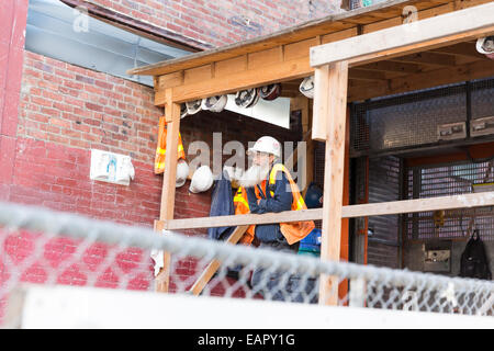 Operaio edile indossando un arancio brillante giubbotto di sicurezza e di elmetto, con lunghi capelli grigi barba, prendendo una pausa Foto Stock