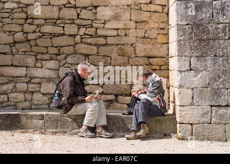 Prendendo una pausa dal Touring. Due persone di mezza età i turisti si prendono una pausa sul banco di pietra al di sotto della parete di asilo e controllare una brochure Foto Stock