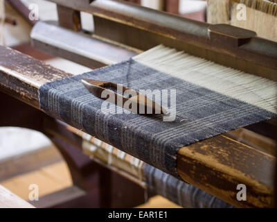 Volano su un intreccio di tartan. Un volano con lana blu poggia su un Tartan pezzo di tessuto in lavorazione su un vintage home telaio. Foto Stock