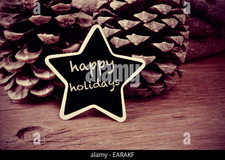 Il testo happy holidays scritto in una configurazione a stella blackboard e alcune pigne nelle quali su una tavola in legno rustico, in bianco e nero Foto Stock