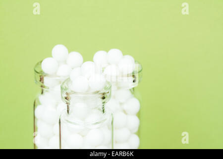 Primo piano immagine di medicinali omeopatici pillole (costituito da una sostanza inerte - zucchero/lattosio) in bottiglie su uno sfondo verde. Foto Stock