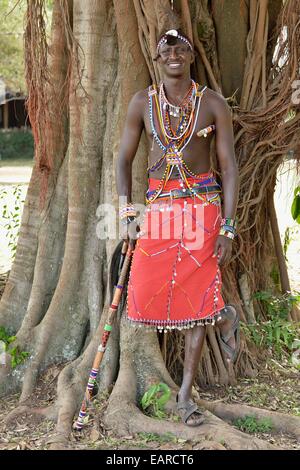 Guerriero masai indossando vestiti tradizionali e in piedi in una tipica posa su una gamba, vicino Enkutoto, Masai Mara Foto Stock