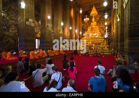 I turisti guarda i monaci buddisti pregano prima di un Buddha d'oro in un tempio. Foto Stock