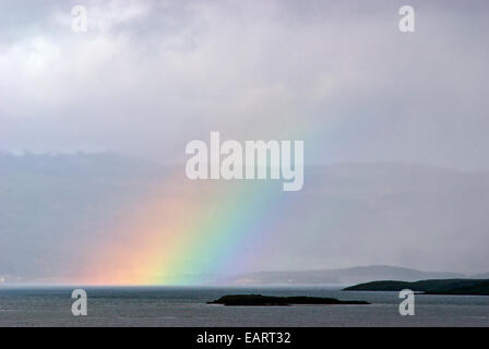 Un arcobaleno sorge dalla superficie oceanica al di sopra di una piccola isola rocciosa. Foto Stock