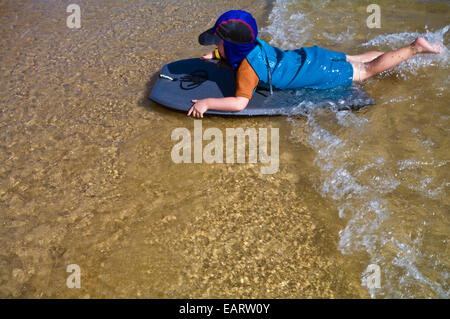 Un giovane ragazzo corse una sponda di cassone su onde nei bassifondi presso la spiaggia. Foto Stock