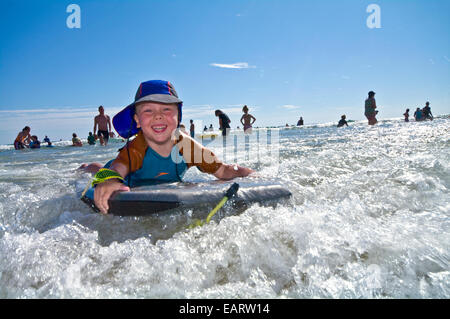 Ridere un giovane ragazzo corse una sponda di cassone nelle onde sulla spiaggia. Foto Stock