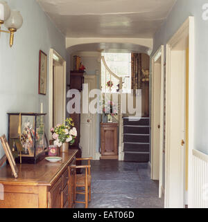 Un tradizionale corridoio che conduce ad una scala con un pavimento di pietra e ornamenti su un lato in legno cabinet, UK. Foto Stock