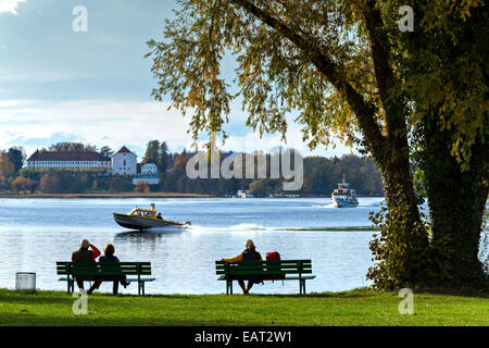 Giovane seduto su un sedile a panchina guardando un Chiemsee barca taxi passano, Fraueninsel, Chiemsee, Chiemgau, Alta Baviera, Deutschland, l'Europa. Foto Stock