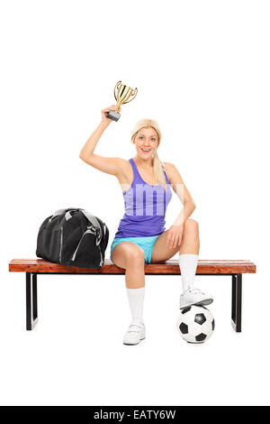 Calcio femminile player tenendo un trofeo seduto su una panchina isolata su sfondo bianco Foto Stock