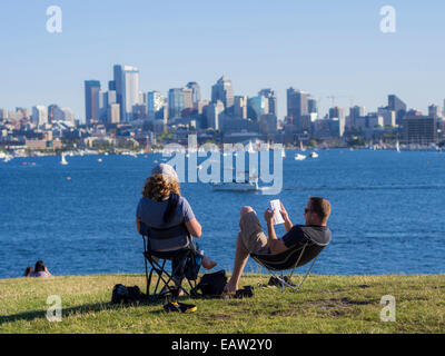 Una coppia siede a leggere al gas Works Park mentre le barche passano davanti al lago Union in una calda giornata estiva a Seattle, Washington. Foto Stock