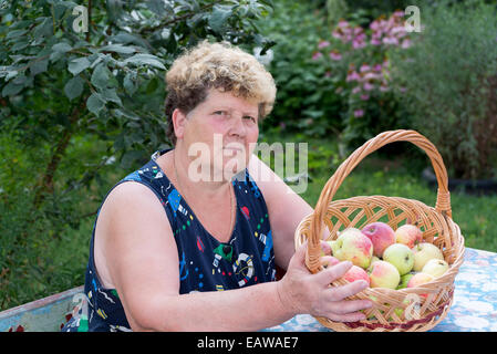 Donna anziana con cesto di mele in giardino Foto Stock