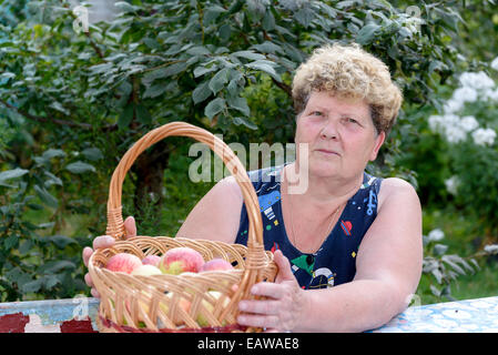 Donna anziana con cesto di mele in giardino Foto Stock