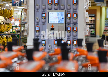 Carrelli per supermercati di fronte a un rack con un palmare subito self-dispositivi di scansione in un supermercato Migros di Zurigo, Svizzera. Foto Stock