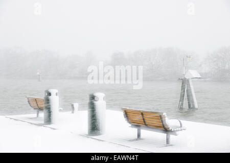 La caduta della neve sulle panchine in corrispondenza del bordo di un fiume Foto Stock