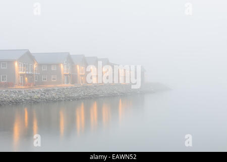 Fila di case lungo un lago in una serata di nebbia Foto Stock