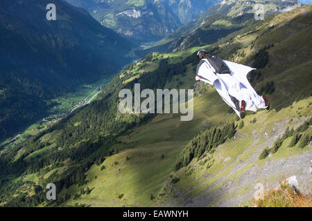 Ponticello di base sta uscendo da una rupe verso il basso nella profonda valle. In tal modo egli è entro una wingsuit a tariffa volare lontano dalla roccia. Foto Stock