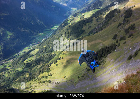 Ponticello di base sta uscendo da una rupe verso il basso nella profonda valle. In tal modo egli è entro una wingsuit a tariffa volare lontano dalla roccia. Foto Stock