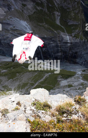 Ponticello di base sta uscendo da una rupe verso il basso nella profonda valle. In tal modo egli è entro una wingsuit a tariffa volare lontano dalla roccia. Foto Stock