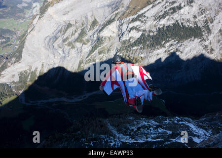 Ponticello di base sta uscendo da una rupe verso il basso nella profonda valle. In tal modo egli è entro una wingsuit a tariffa volare lontano dalla roccia. Foto Stock