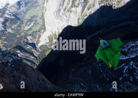 Ponticello di base sta uscendo da una rupe verso il basso nella profonda valle. In tal modo egli è entro una wingsuit a tariffa volare lontano dalla roccia. Foto Stock