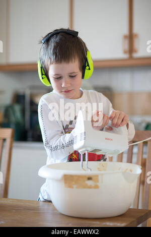 Ragazzo che indossa le cuffie giallo utilizza un mixer elettrico Foto Stock