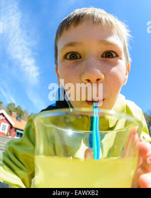 Ragazzo con occhi spalancati beve succo di frutta con una paglia Foto Stock