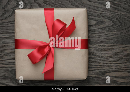 Brown box regalo con fiocco rosso sulla tavola di legno, vista dall'alto Foto Stock