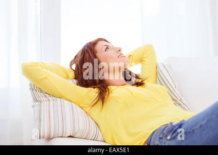 Sorridente giovane donna sdraiata sul divano di casa Foto Stock