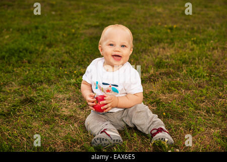 Sorridente bellissimo bambino guardando la fotocamera e mangiare all'aperto Apple in presenza di luce solare Foto Stock