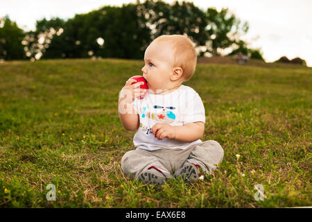 Sorridente bellissimo bambino guardando la fotocamera e mangiare all'aperto Apple in presenza di luce solare Foto Stock