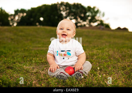 Sorridente bellissimo bambino guardando la fotocamera e mangiare all'aperto Apple in presenza di luce solare Foto Stock