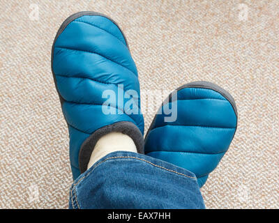 Una donna con i piedi attraversata indossando un paio di jeans e calda imbottitura di pantofole sul tappeto a casa visto da sopra. Inghilterra, Regno Unito, Gran Bretagna Foto Stock